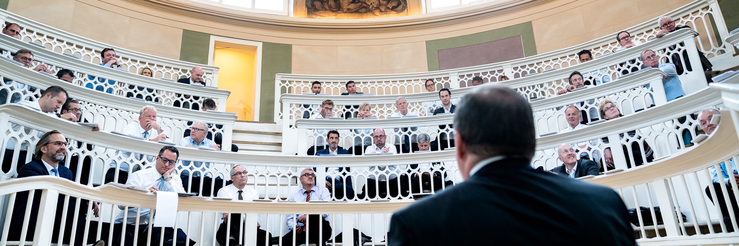 Mitglieder lauschen einem Redner im Rundsaal der VOTUM Mitgliederversammlung